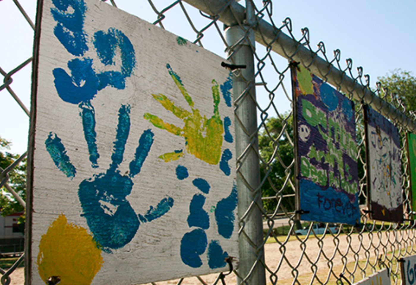 Mural and kids' paintings hanging on a fence at a playground