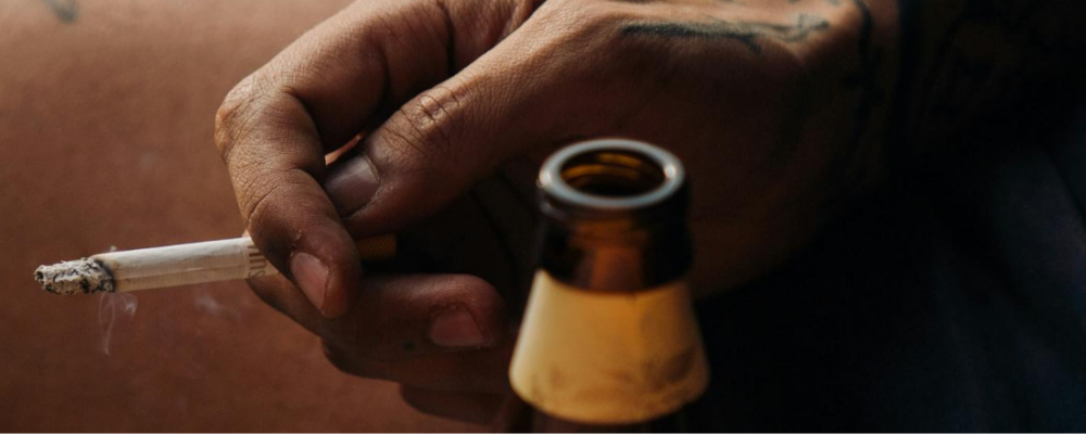 a person holding a cigarette in their hand next to a beer bottle