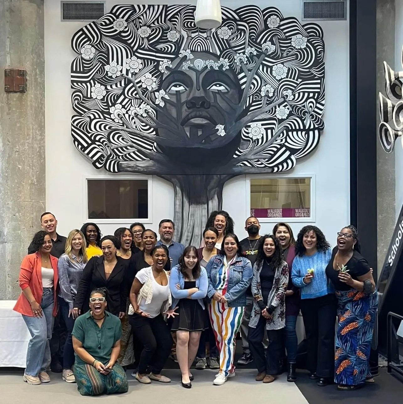 group photo of people smiling in front of mural of tree