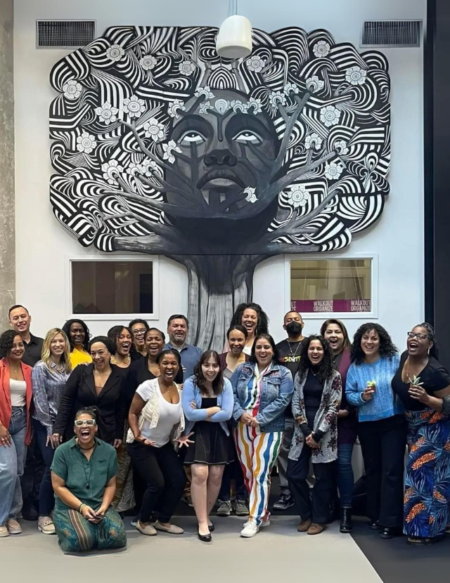 group photo of people smiling in front of mural of tree