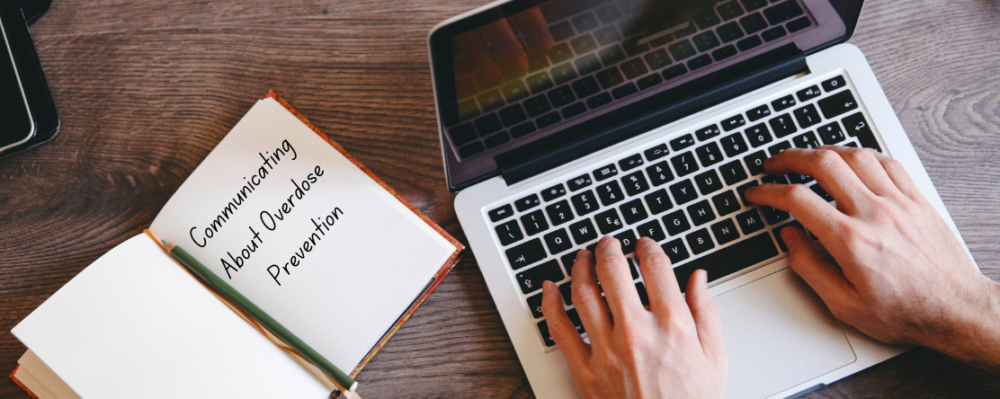 person writing on laptop with notebook that says "Communicating About Overdose PRevention"