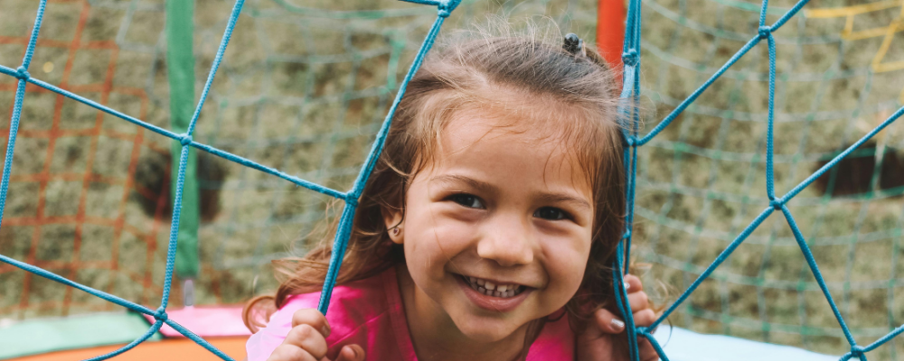 girl smiling and looking through fence on the playground