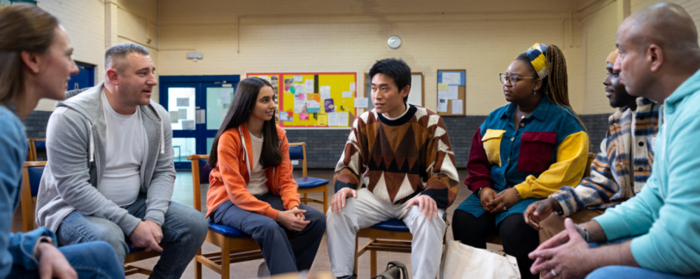 Waist-up shot of adults, sitting in a circle and talking together