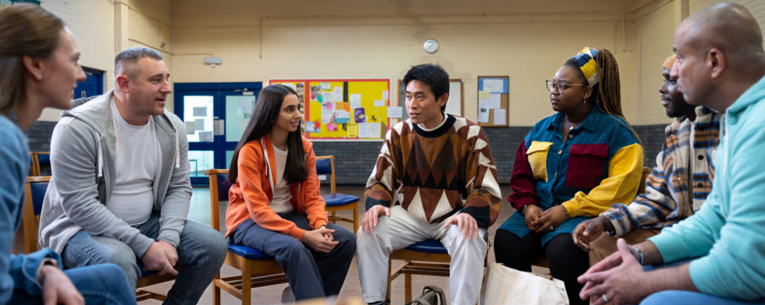 Waist-up shot of adults, sitting in a circle and talking together